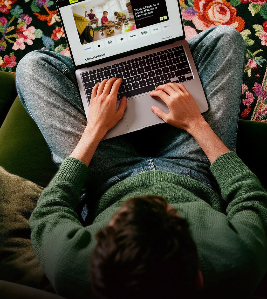 Mâinile unei persoane care navighează pe Nativ de pe un laptop, așezat pe un covor tradițional cu flori.